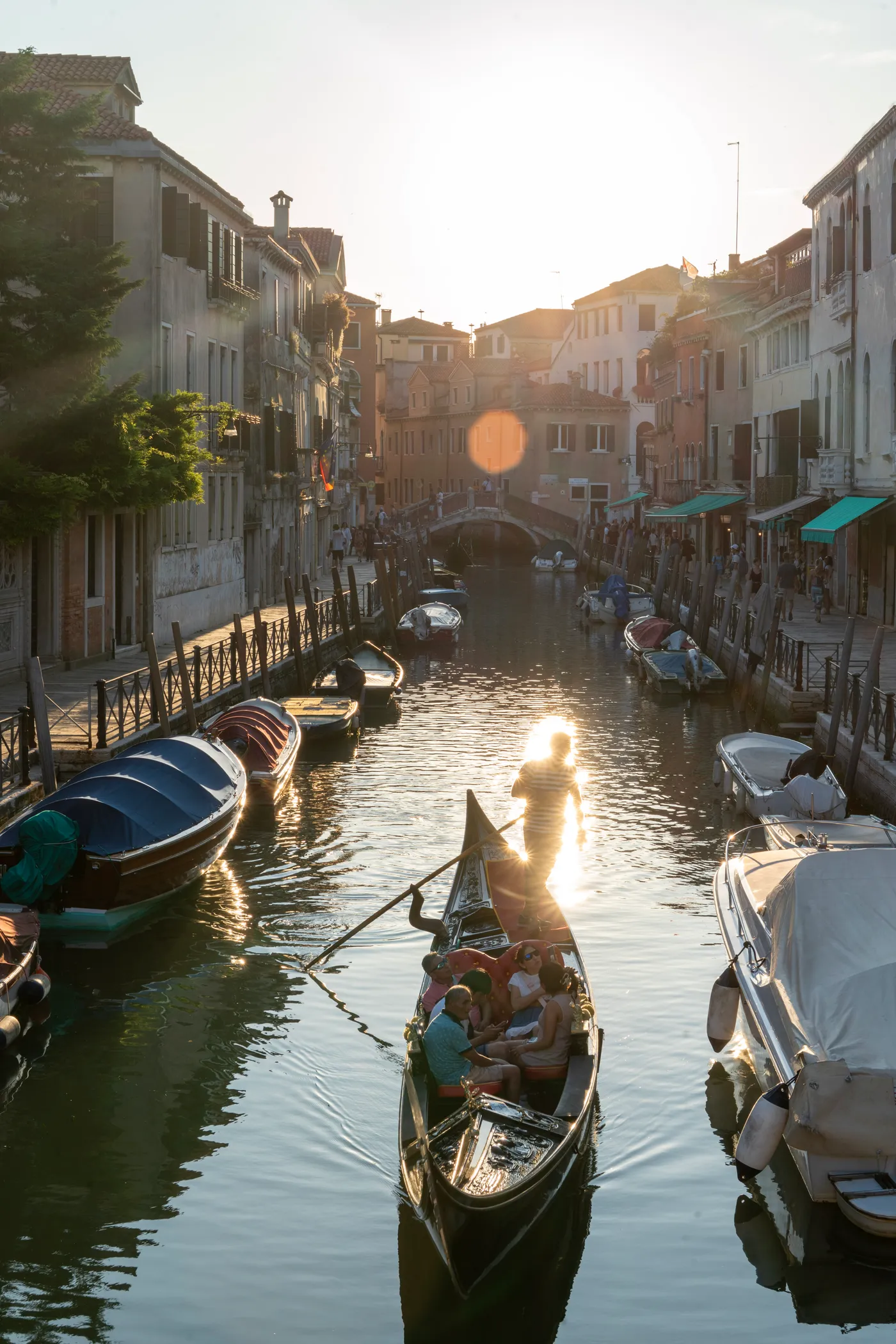 A gondola into the low sun, boats moored along the canal.